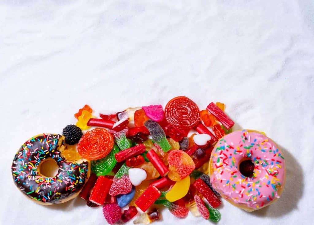 Pile of sugary treats on a bed of white sugar. Sugar detox instructions.